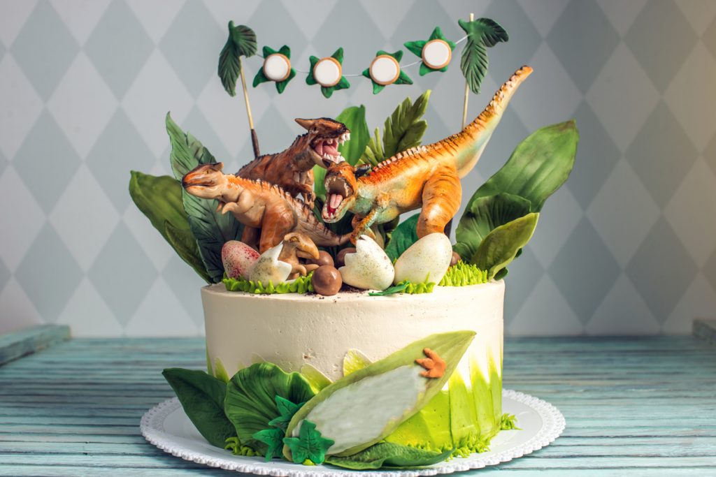 Children's dinosaur birthday cake decorated with mastic figurines of dinosaurs in the Jurassic period jungle