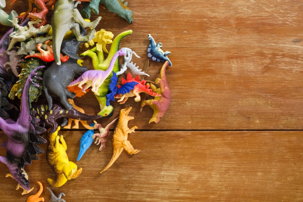 Overhead view of a collection of bright colorful Toy dinosaurs on top of a wooden table.