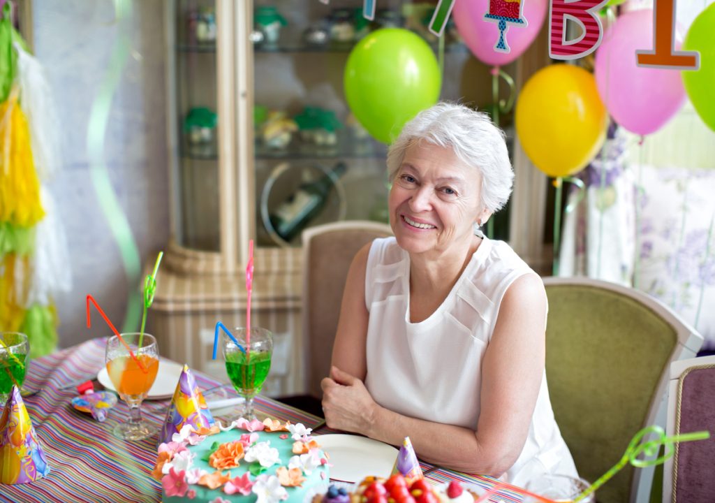 Smiling elderly woman at an 80th birthday party with tropical decorations.