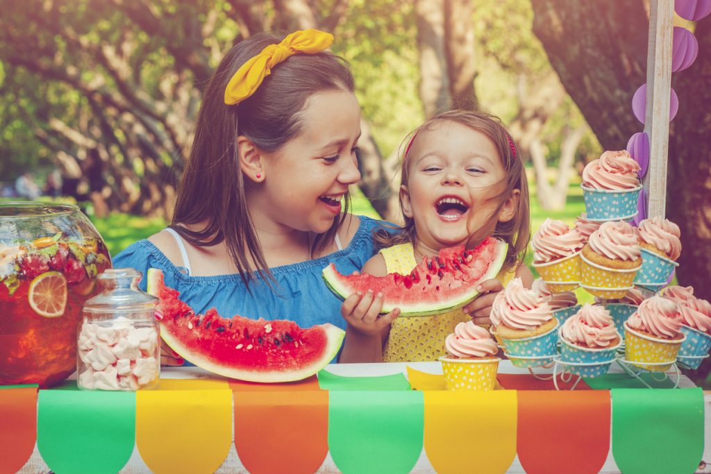 Two sisters having fun outdoors in summer with watermelon, sweets and cupcakes.