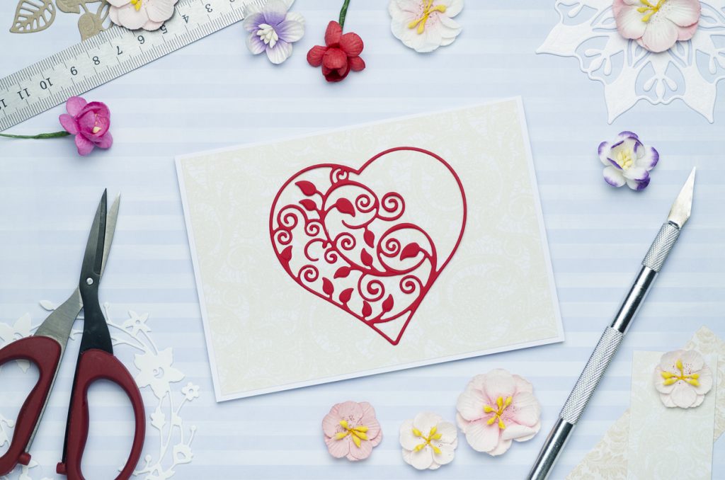 Beautiful red heart cut from paper on a greeting card with paper flowers.