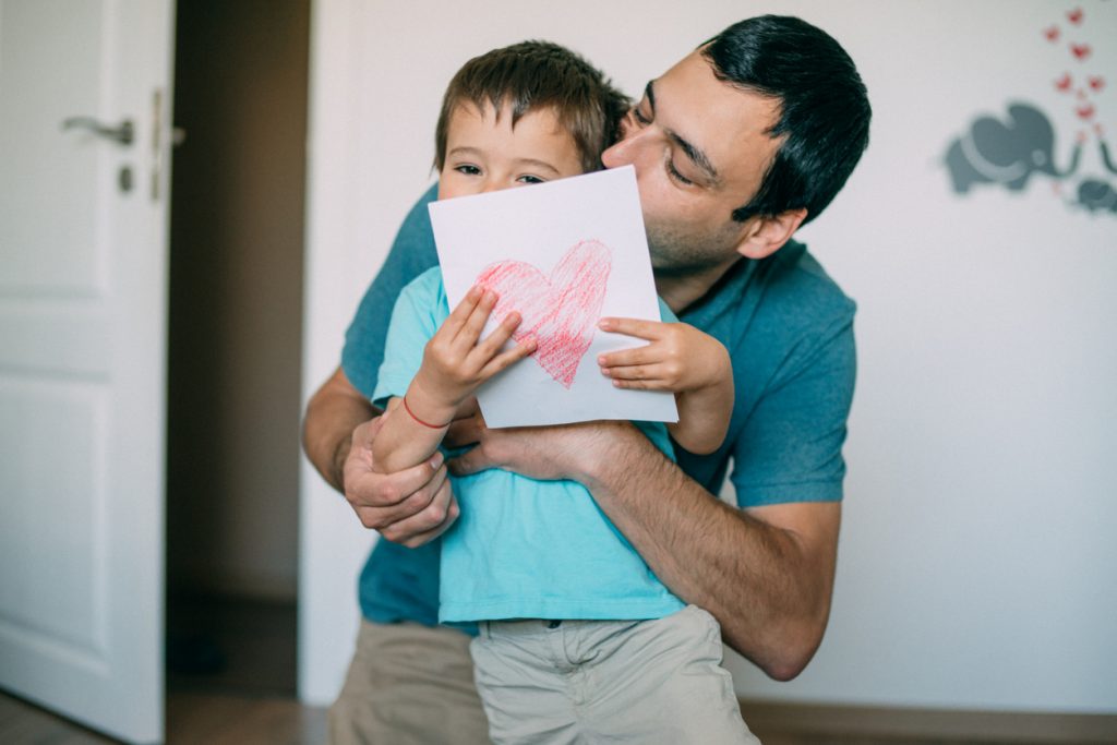 Surprised dad holding handmade greeting card and embracing his smiling child.