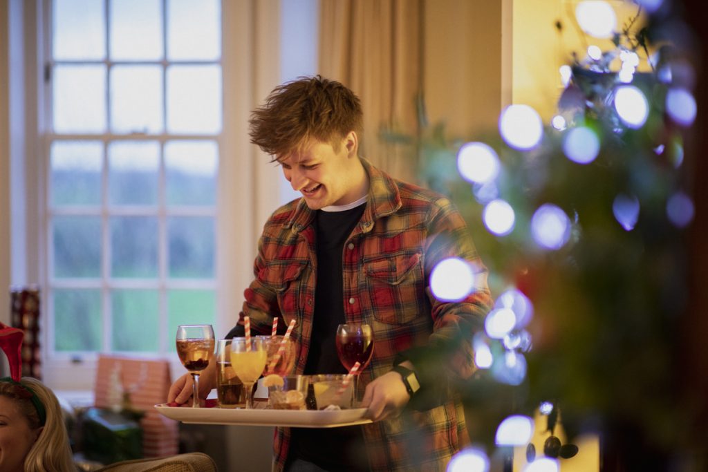 One young man is serving drinks to his friends at a Christmas house party.
