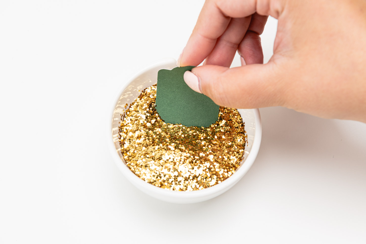 someone dipping the gift tag into a bowl of gold glitter.