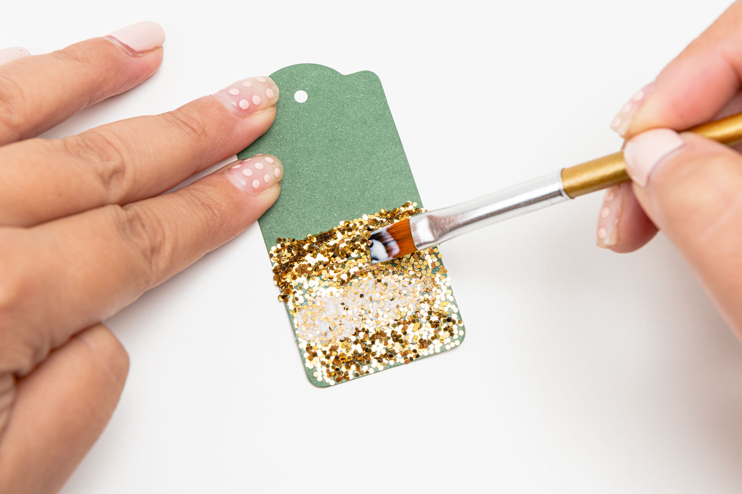 someone brushing over glitter on a gift tag with a paintbrush.