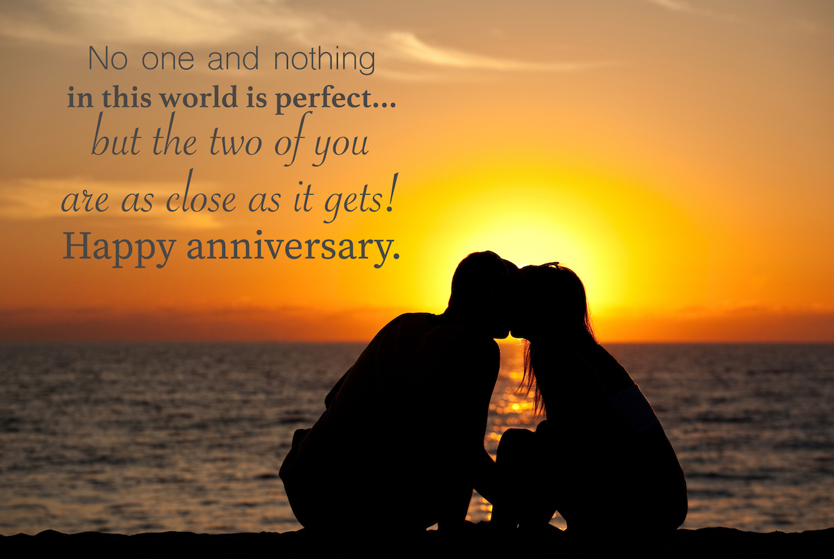 A romantic couple sitting on a beautiful beach kissing. Silhouette with anniversary wishes overlay.