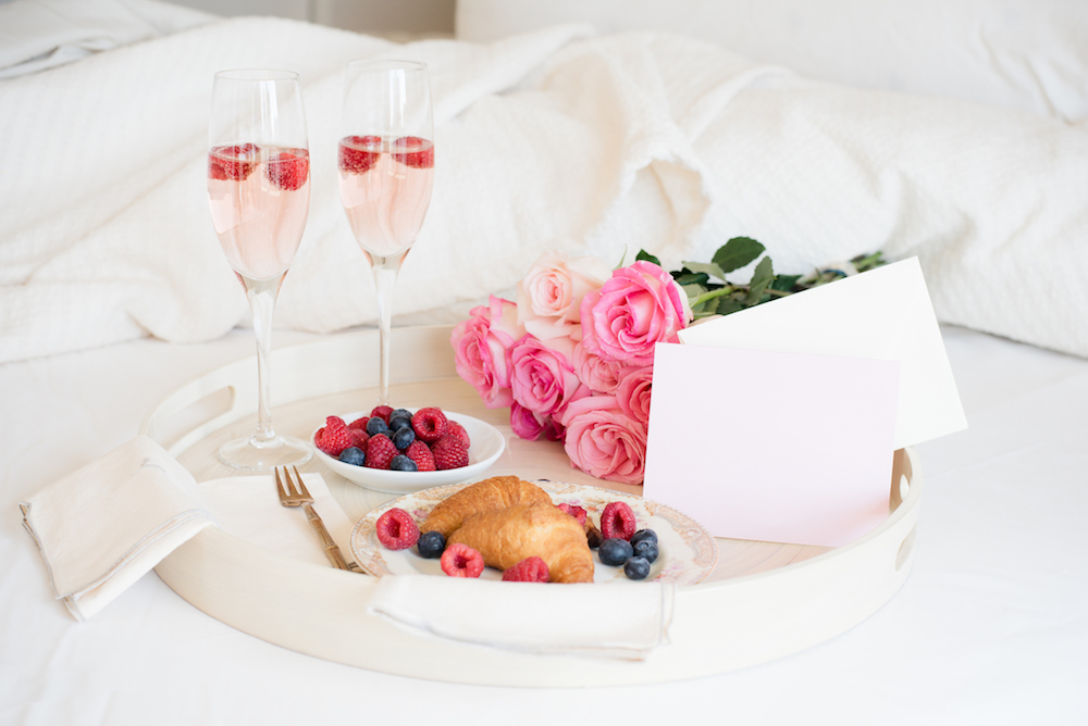 Flat lay of flowers and food on tray on a bed with mimosas
