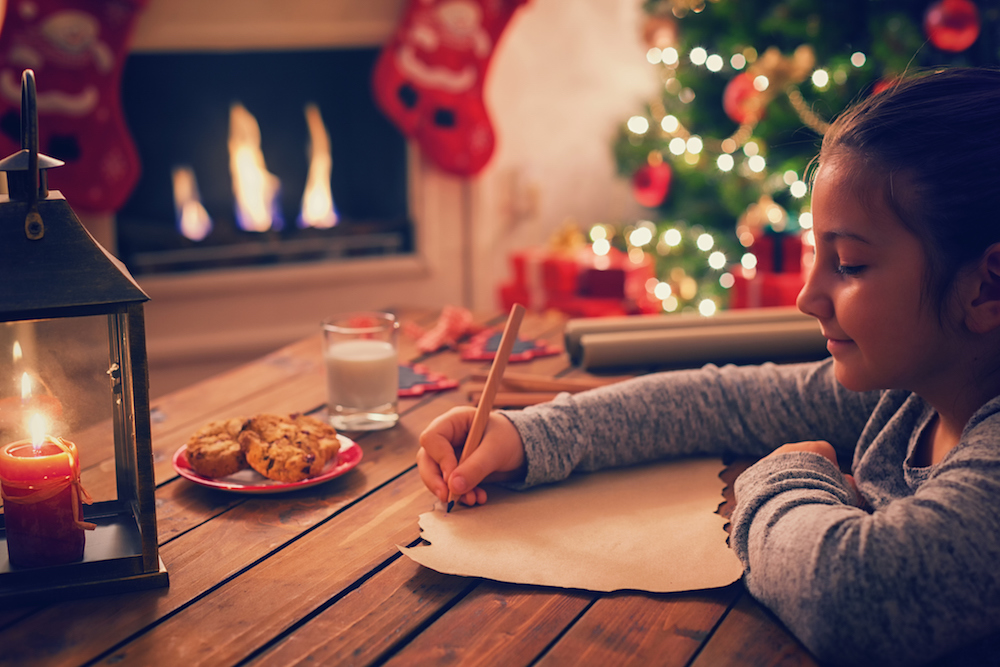 Young girl writing Christmas list ideas by a fire