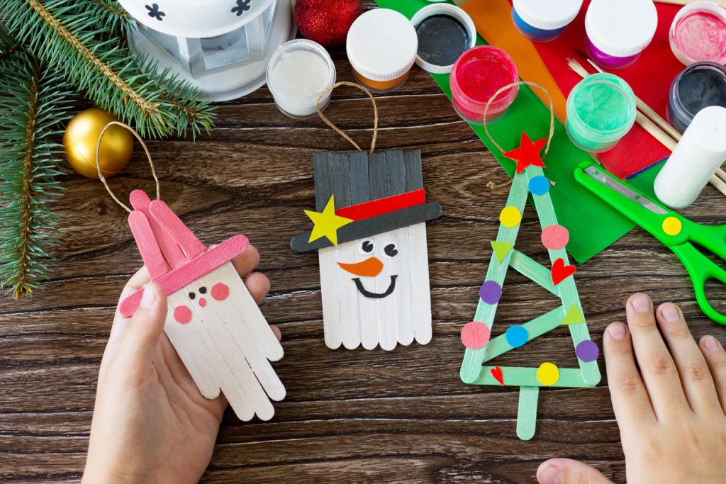 A child is holding Christmas craft of wooden sticks. 