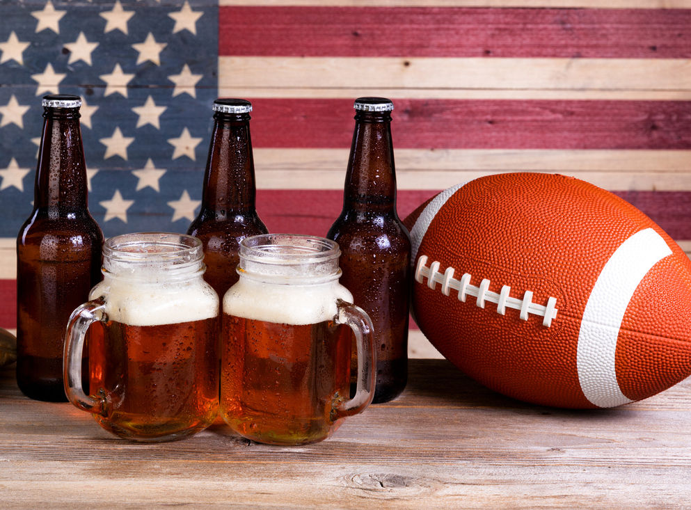 Two pint jars filled with beer, full bottles, football and baseball mitt with vintage wooden USA flag in background. (Two pint jars filled with beer, full bottles, football and baseball mitt with vintage wooden USA flag in background., ASCII, 117 comp