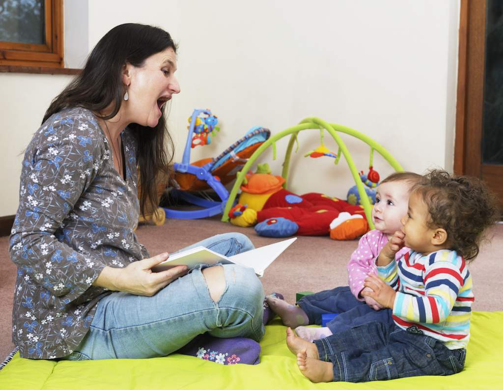 A woman reads a story to a group of babies as one of her playdate ideas