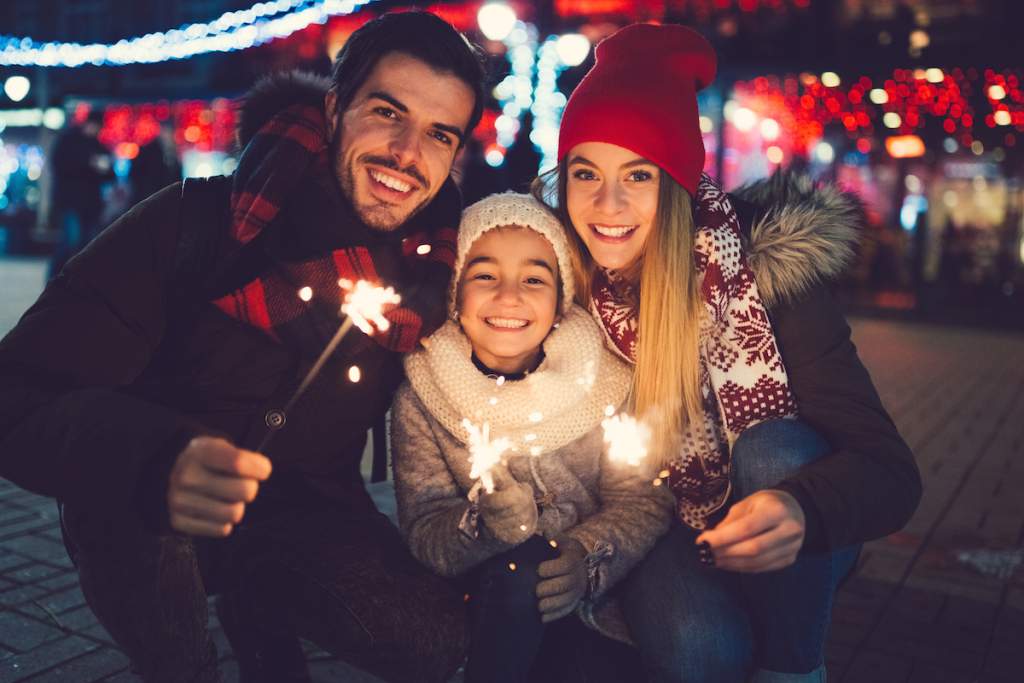 Family with one kid holding burning sparklers and looking at camera during Christmas as an exaple of portrait photography