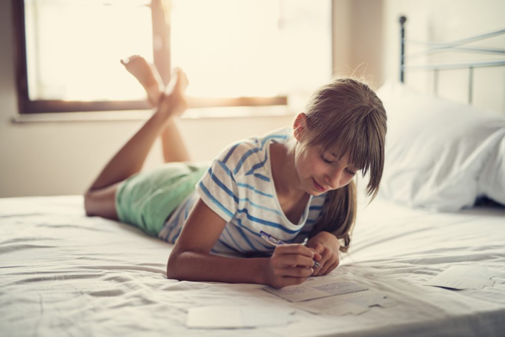 Teenage girl lying on bed and writing her kids thank you notes.