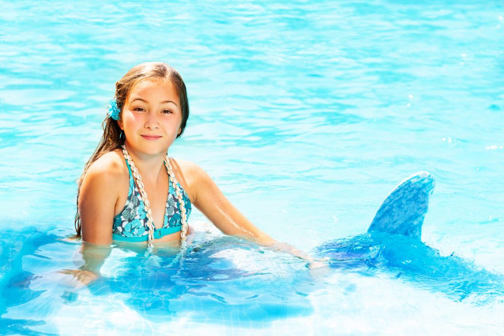 Portrait of birthday girl in mermaid costume relaxing in blue water of swimming pool