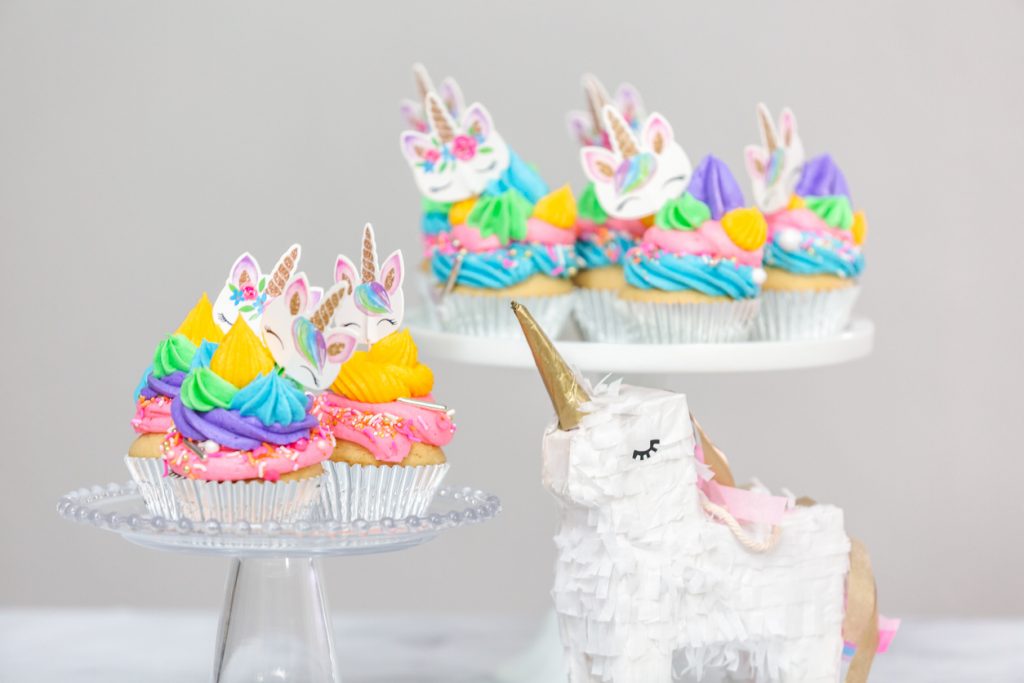 Unicorn piñata and cupcakes with multicolor buttercream icing on cake stands.