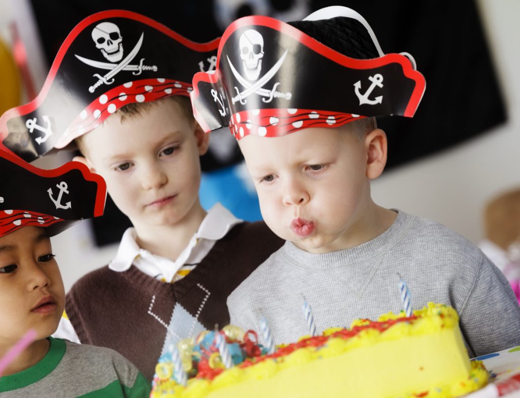 A group of boys dressed in pirate hats celebrate at a birthday party.
