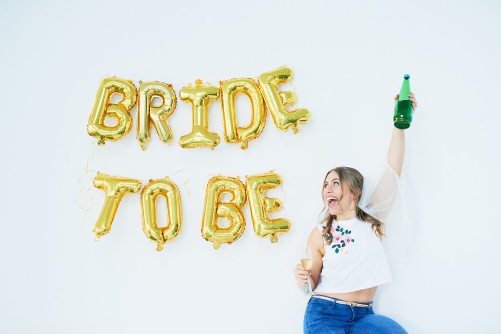 Woman celebrating her engagement with “bride to be” in balloons on the wall.