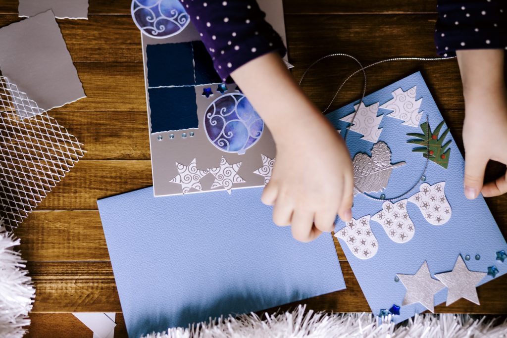 Little girl making Christmas cards on wooden background.
