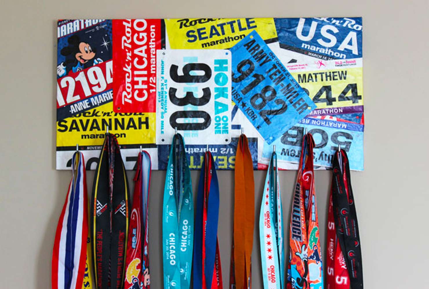Bulletin board of race bibs with medals hanging on hooks.