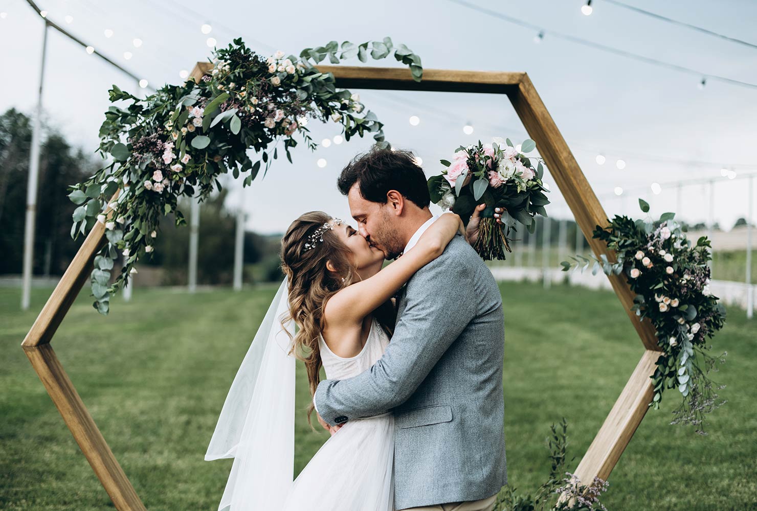 Bride and groom kissing under hexagon arch.