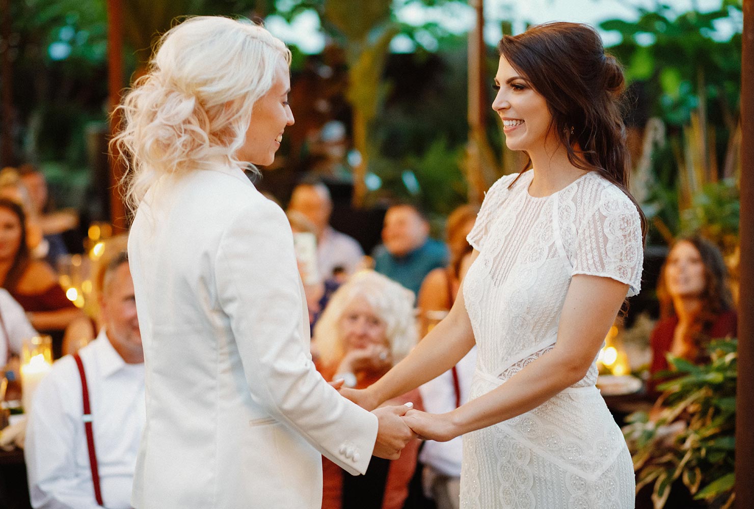 Two brides smiling and holding hands at wedding