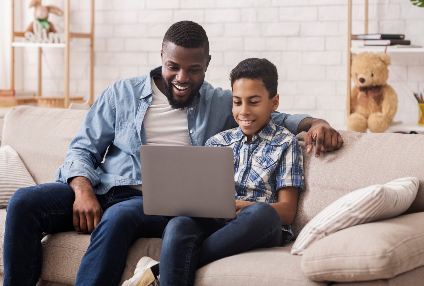 Young boy and Dad sitting on couch smiling at laptop
