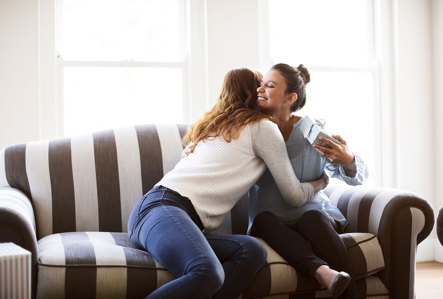 Two women hugging on couch. 