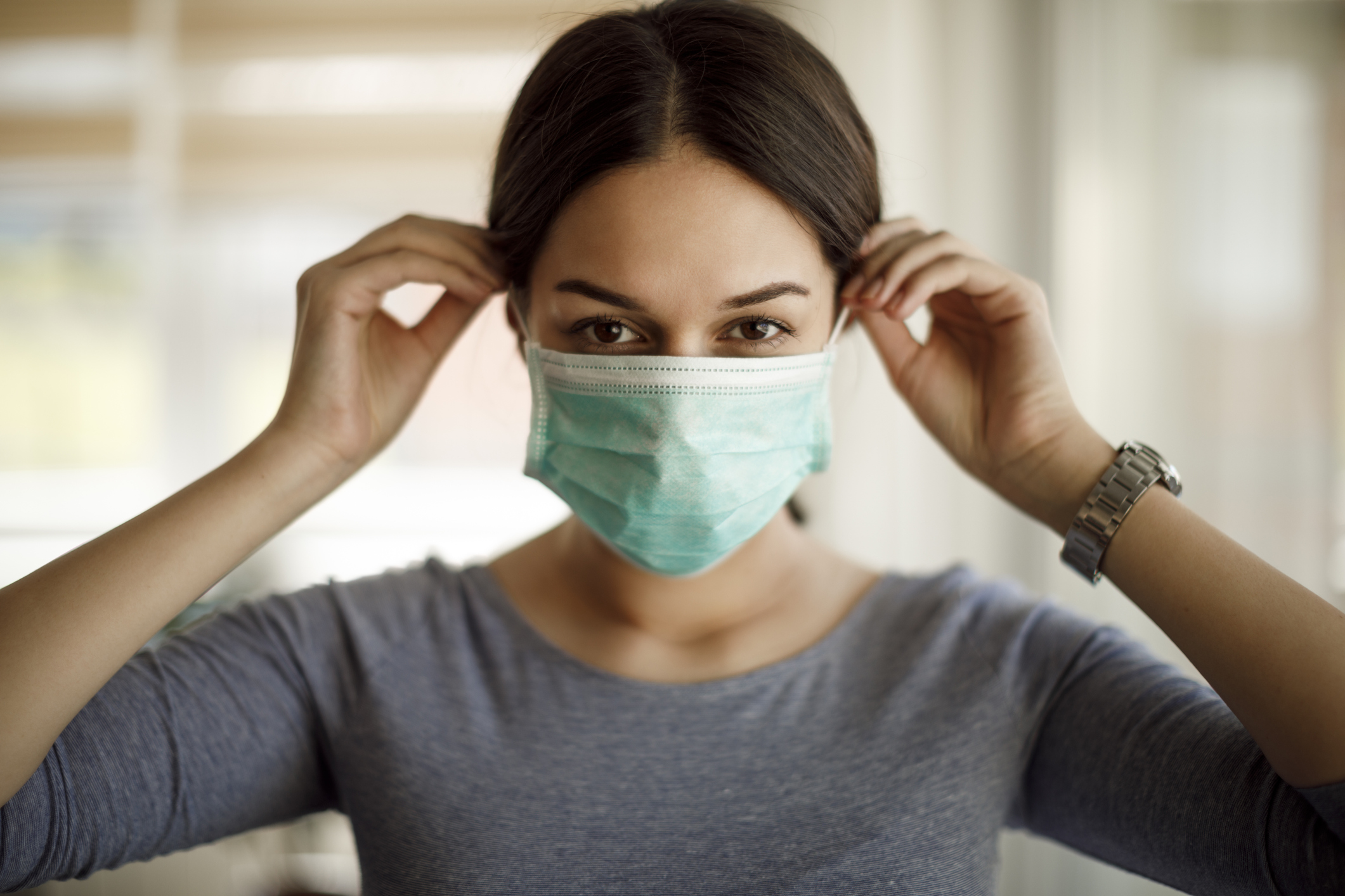 woman putting on a protective face mask to prevent the spread of coronavirus