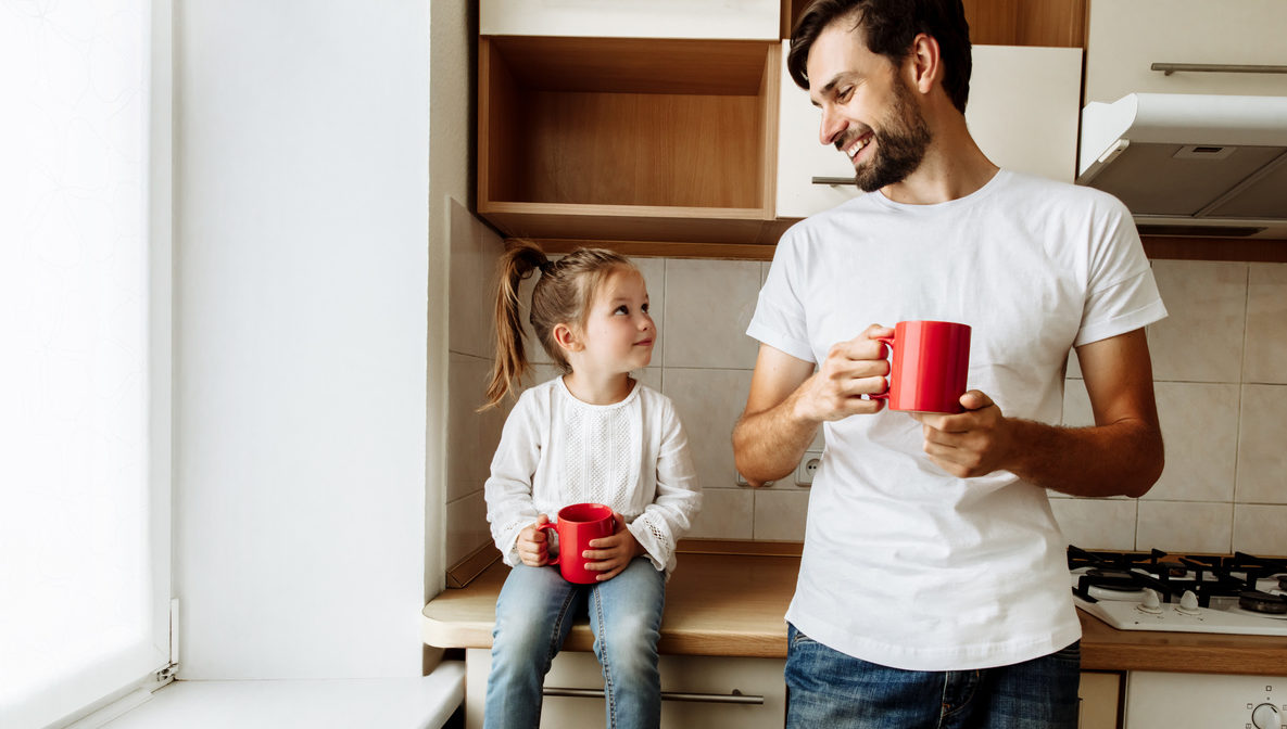 Parenthood. Family. Love. Dad and his little daughter are holding red cups, looking at each other and smiling. In the kitchen at home